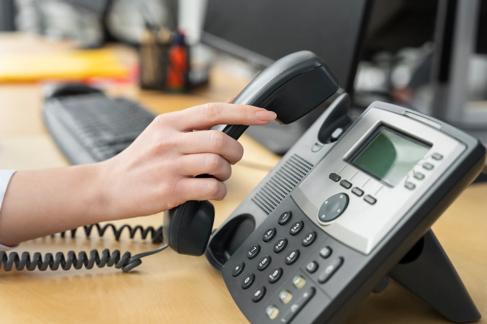 A hand picking up the handset of an office desk phone